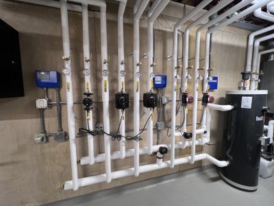 Insulated white-jacketed pipe manifold with gauges and control boxes installed by Metro Insulation Rows of white insulated pipes with gauges and blue control boxes on a mechanical room wall