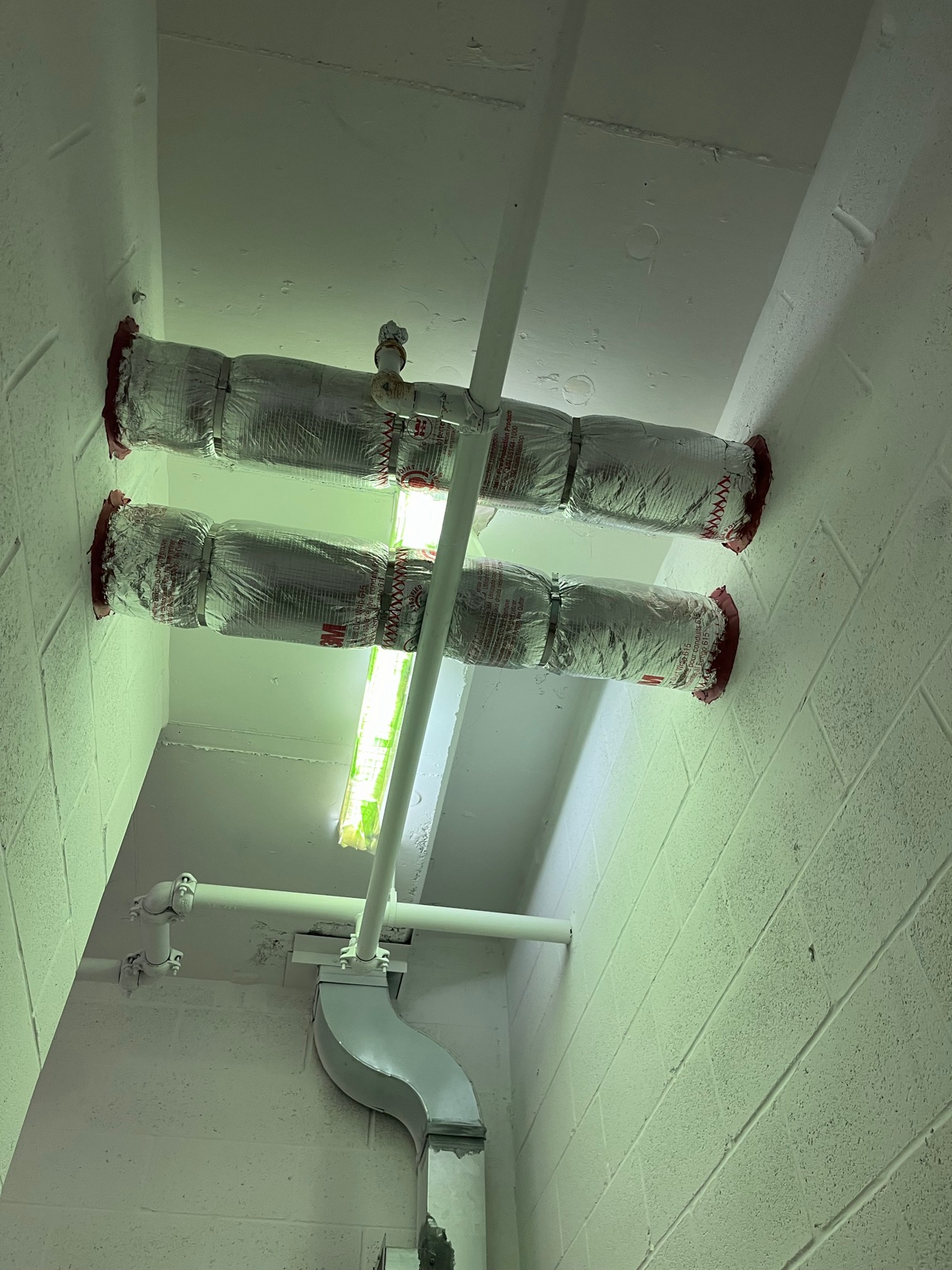 Foil-faced insulated pipe with red firestop caulk at a concrete wall penetration installed by Metro Insulation Fire-rated pipe wrap on silver foil-faced insulated pipes with red fire barrier sealant at concrete wall penetrations, installed by Metro Insulation in a Toronto high-rise