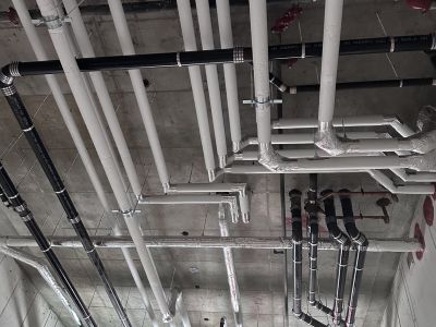 Insulated white-jacketed pipe runs across a concrete ceiling installed by Metro Insulation White-jacketed insulated pipes running across a concrete ceiling with red fittings and fire-rated pipe wrap below