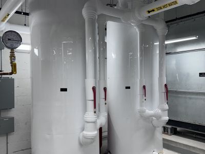 White-jacketed domestic hot and cold water pipe runs with yellow labels installed by Metro Insulation White insulated domestic hot and cold water pipes with yellow DOM HOT WATER labels running across a ceiling