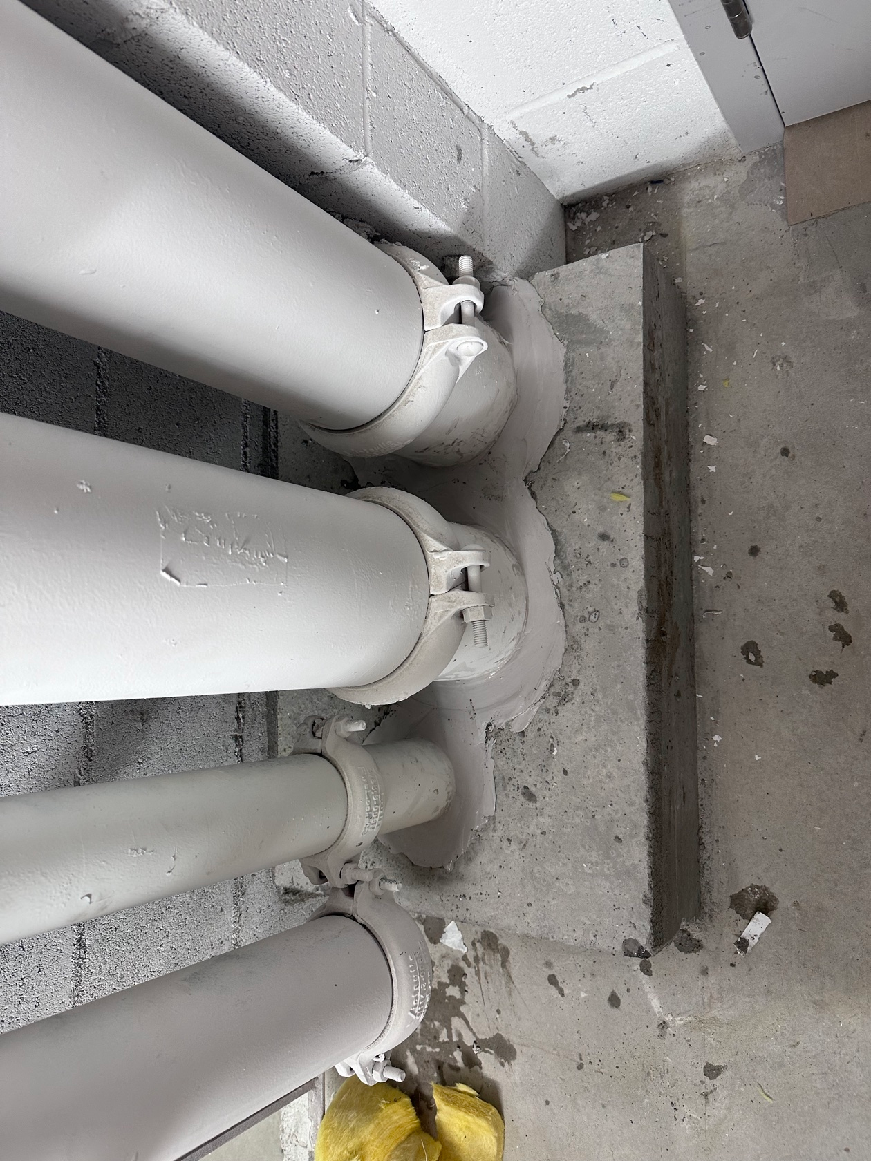af6d93ae59658064a110ef012ccbfda75e09dfe2800731fd90f2e11c66f072ee Firestopping sealant around white mechanical pipes with grooved couplings penetrating a concrete wall, installed by Metro Insulation in a Toronto high-rise