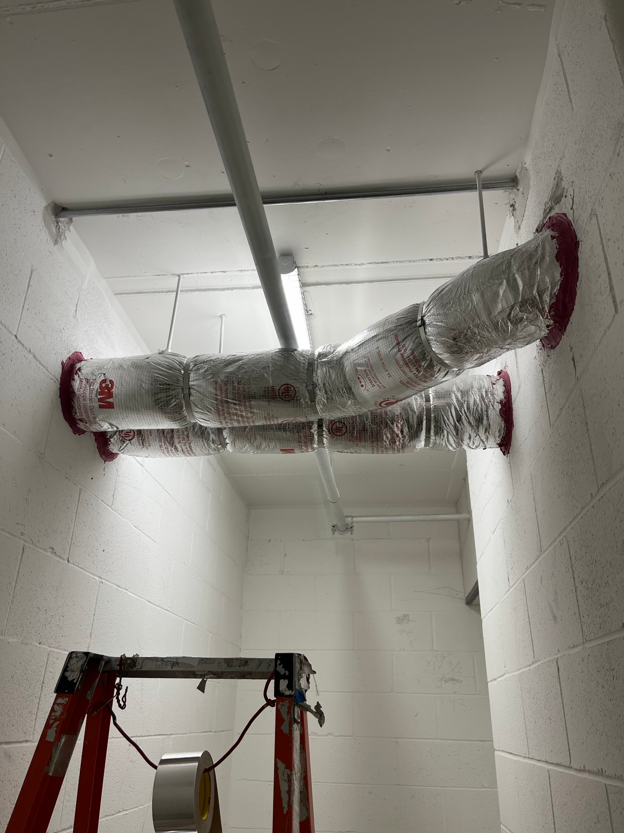 Red firestop caulk sealing a pipe penetration through a concrete wall installed by Metro Insulation Fire-rated pipe wrap with red fire barrier sealant at a pipe penetration through a concrete wall, installed by Metro Insulation in a Toronto high-rise