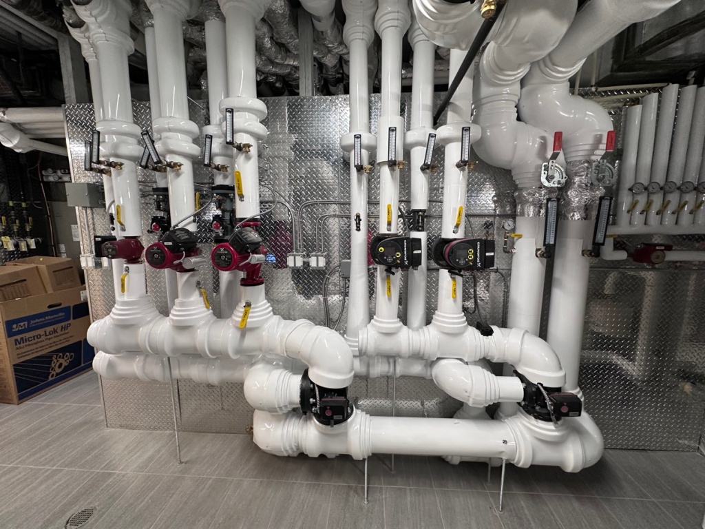 Insulated white-jacketed pipe runs installed by Metro Insulation in a Toronto high-rise mechanical room White-jacketed insulated pipe runs with thermometers and red circulator pumps in a mechanical room