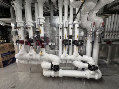Insulated white-jacketed pipe runs installed by Metro Insulation in a Toronto high-rise mechanical room White-jacketed insulated pipe runs with thermometers and red circulator pumps in a mechanical room
