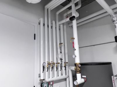 White PVC-jacketed insulated pipe runs with fabricated elbows across a ceiling installed by Metro Insulation White PVC-jacketed insulated pipe runs with fabricated elbows crossing over each other across a ceiling