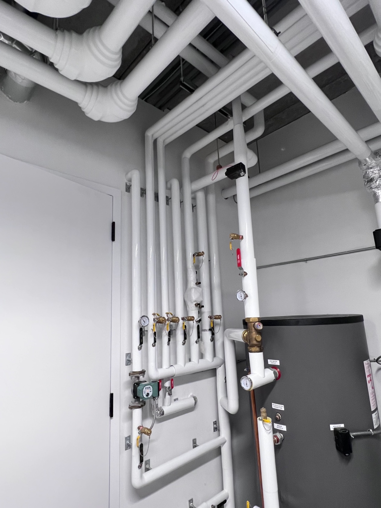 White PVC-jacketed insulated pipe runs with fabricated elbows across a ceiling installed by Metro Insulation White PVC-jacketed insulated pipe runs with fabricated elbows crossing over each other across a ceiling