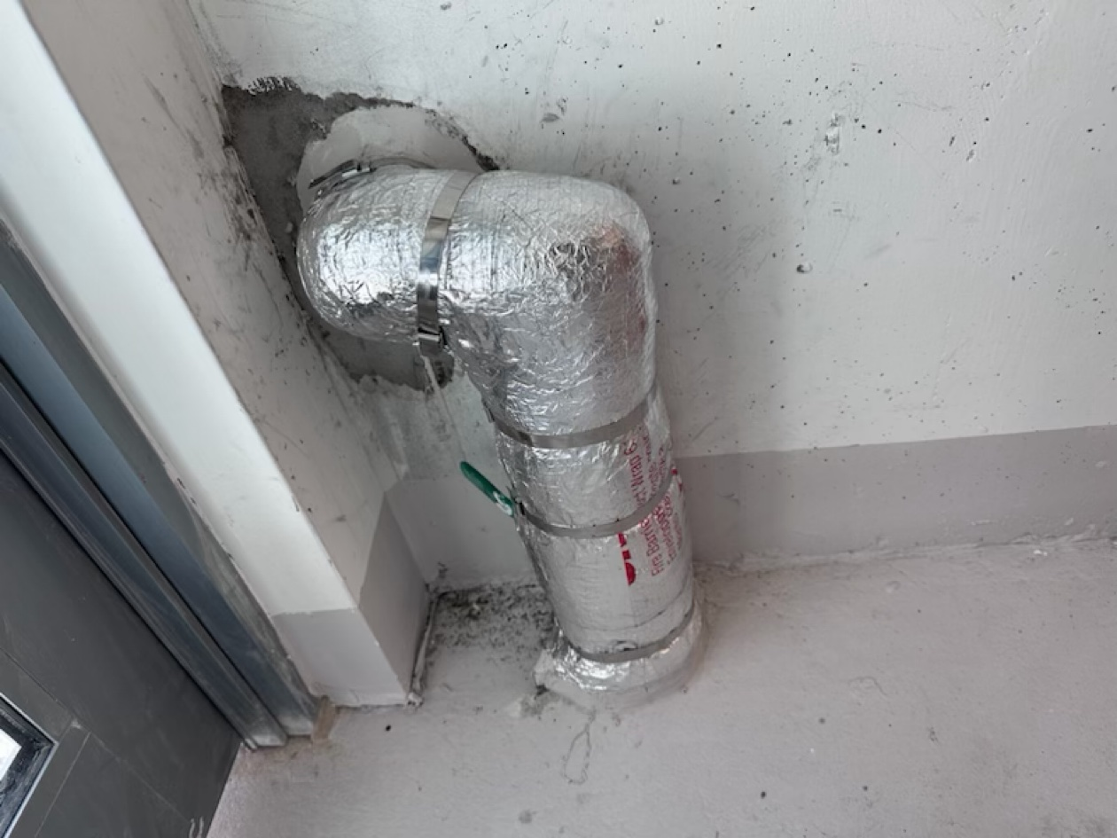 d62ec786ef109a239a412cef20f2d7ffc491b361abcfcee835bdc9940a28b03c Fire-rated pipe wrap on a foil-faced fire barrier wrapped pipe elbow and riser in a corner, with red 3M Fire Barrier print visible, installed by Metro Insulation in a Toronto high-rise