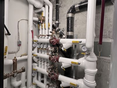 White PVC-jacketed insulated pipe elbows along a concrete wall installed by Metro Insulation White PVC-jacketed insulated pipe elbows running along a concrete wall beside fire-rated pipe wrap