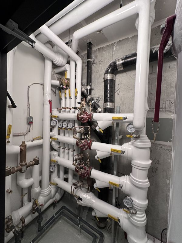 White PVC-jacketed insulated pipe elbows along a concrete wall installed by Metro Insulation White PVC-jacketed insulated pipe elbows running along a concrete wall beside fire-rated pipe wrap