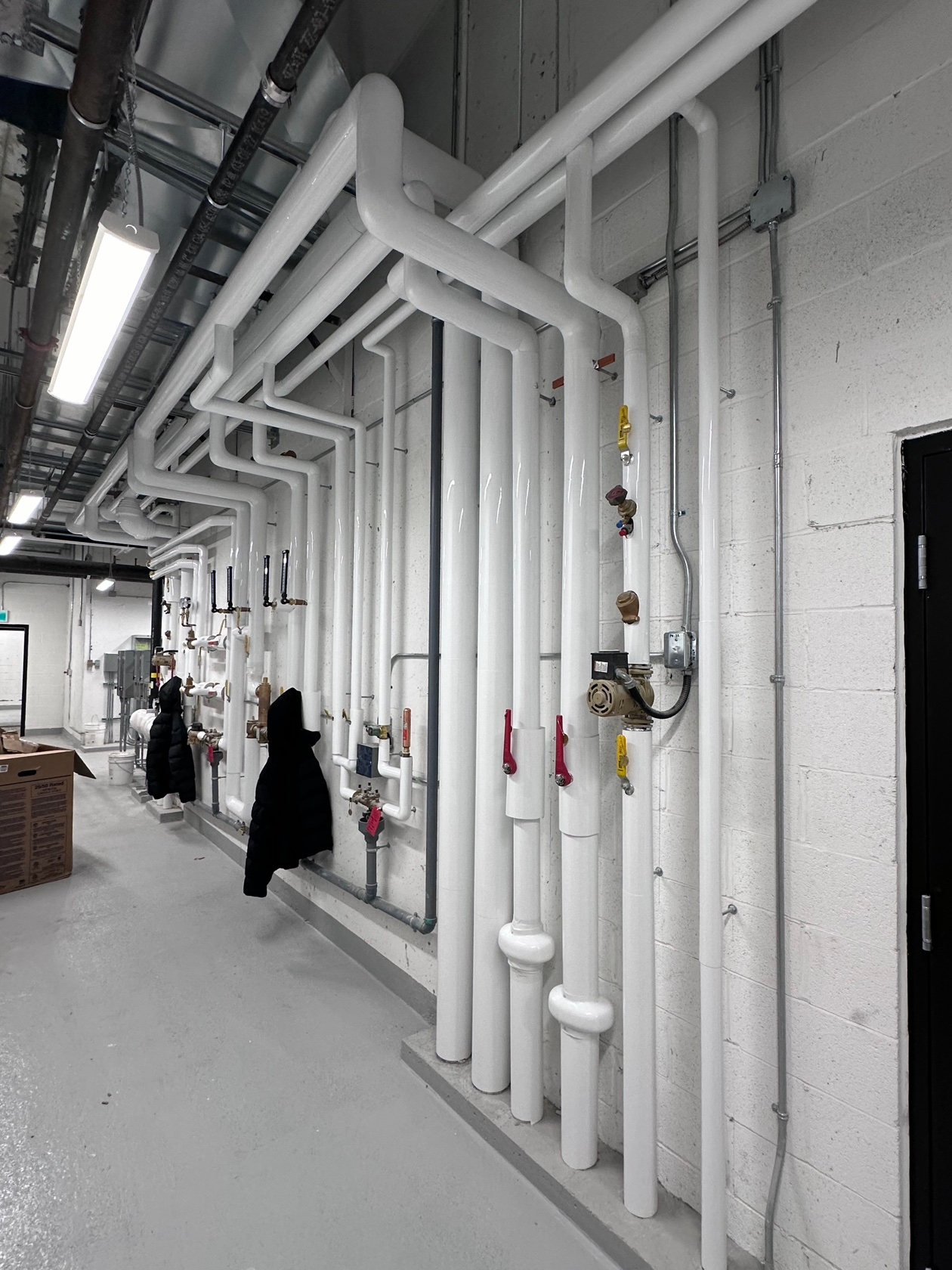 White PVC-jacketed insulated pipes running along a mechanical room wall